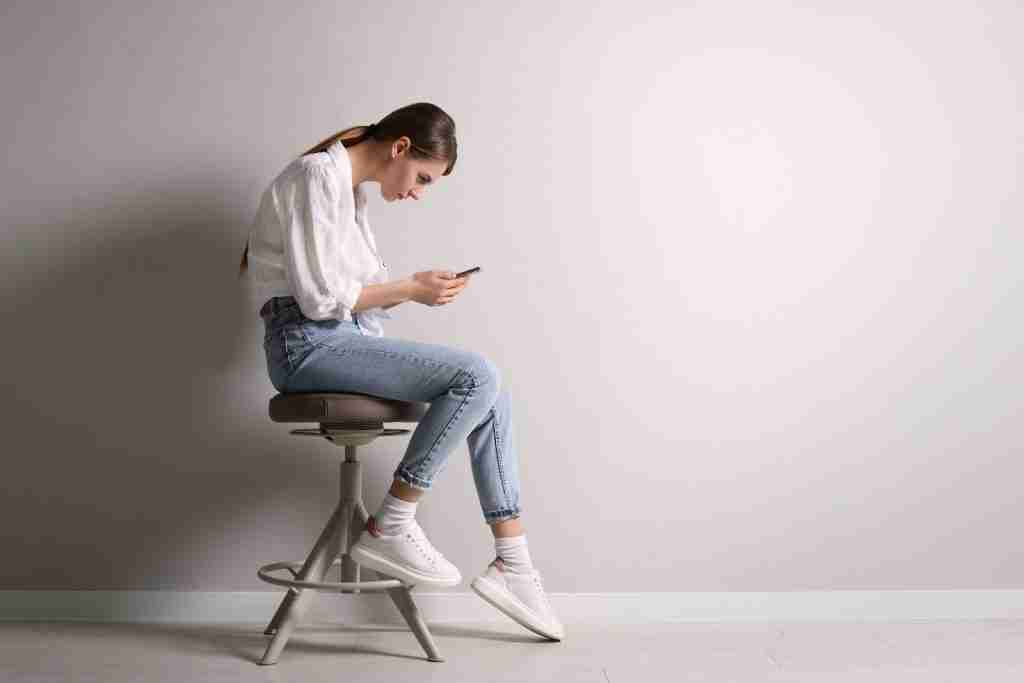 A woman on a stool, focused on her phone, reflecting on back pain and potential chiropractic care solutions.